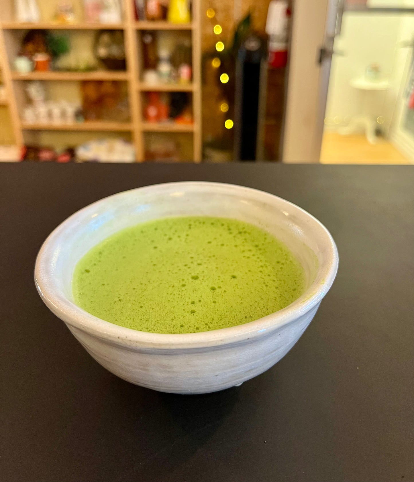 White bowl with green matcha on a dark surface, blurred background