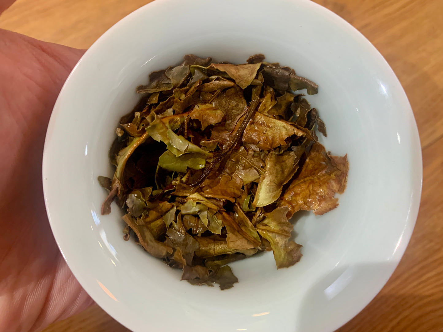 White bowl filled with dried tea leaves held by a hand on a wooden surface