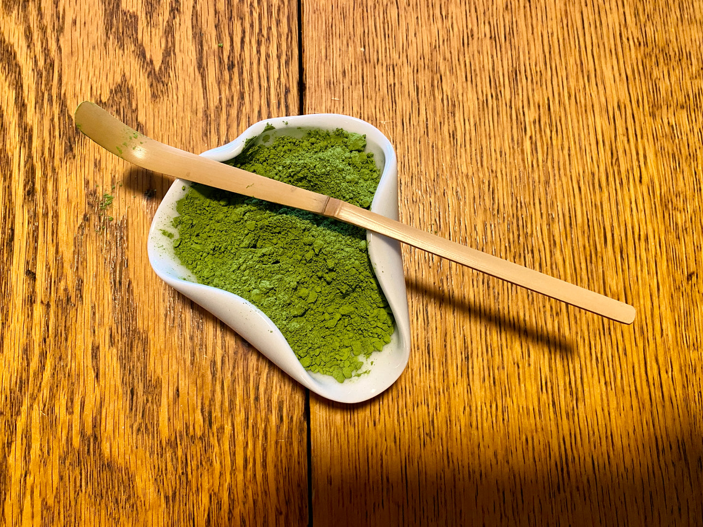Green matcha powder in white bowl with tea scoop