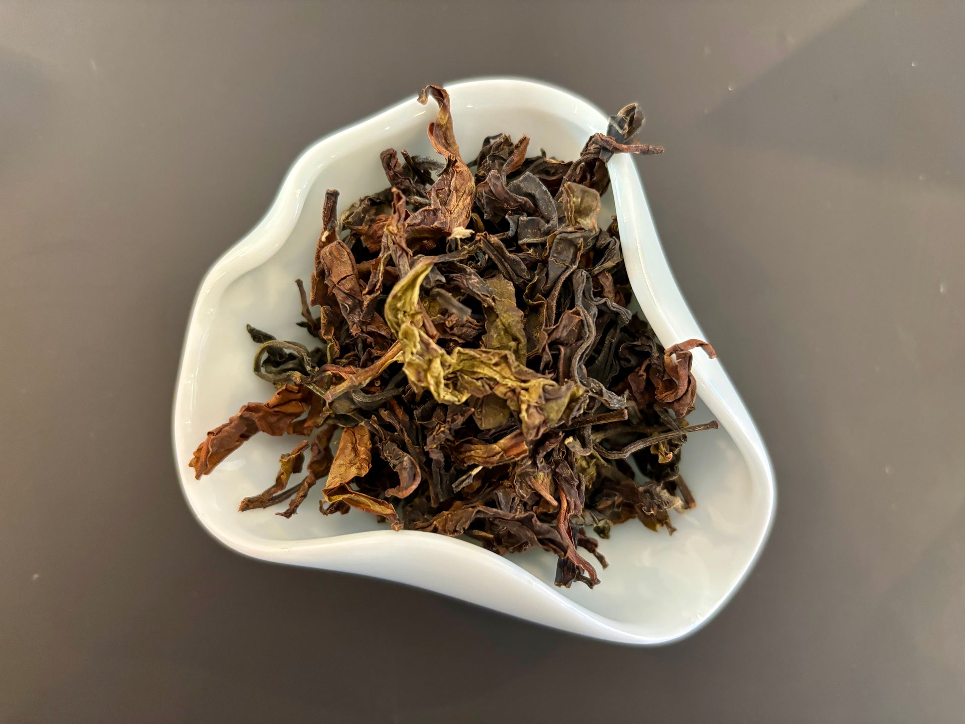 A white bowl filled with dried tea leaves and small twigs, which is Badger's Breakfast Sri Lankan Black Tea.