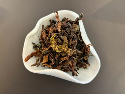 A white bowl filled with dried tea leaves and small twigs, which is Badger's Breakfast Sri Lankan Black Tea.