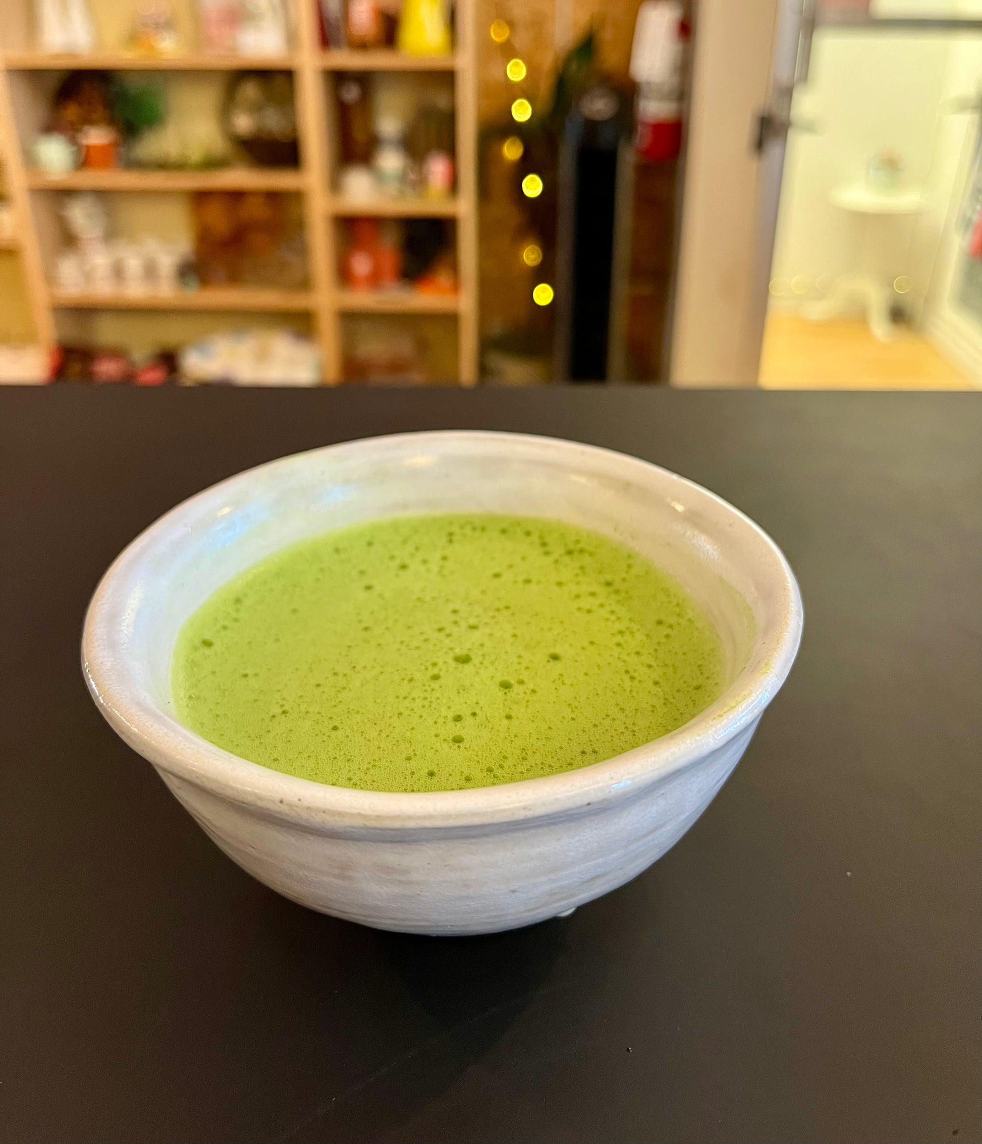 White bowl with green matcha on a dark surface, blurred background