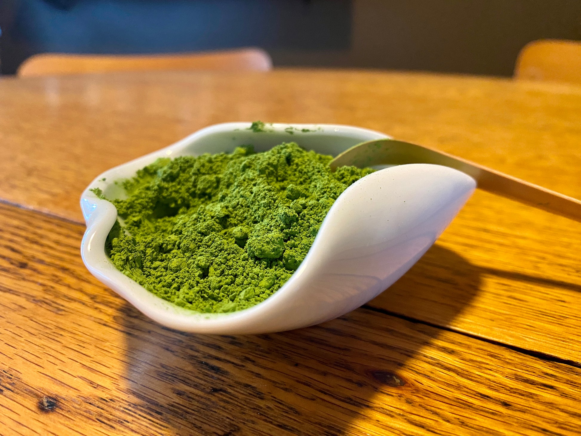 A bowl of green matcha powder on a wooden table, with a spoon resting in the bowl.