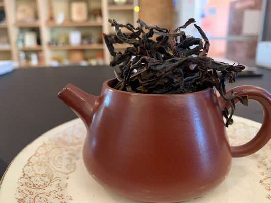 A small yixing teapot filled with dry Huang Zhi Xiang Dancong tea leaves, placed on a white plate with gold patterns.