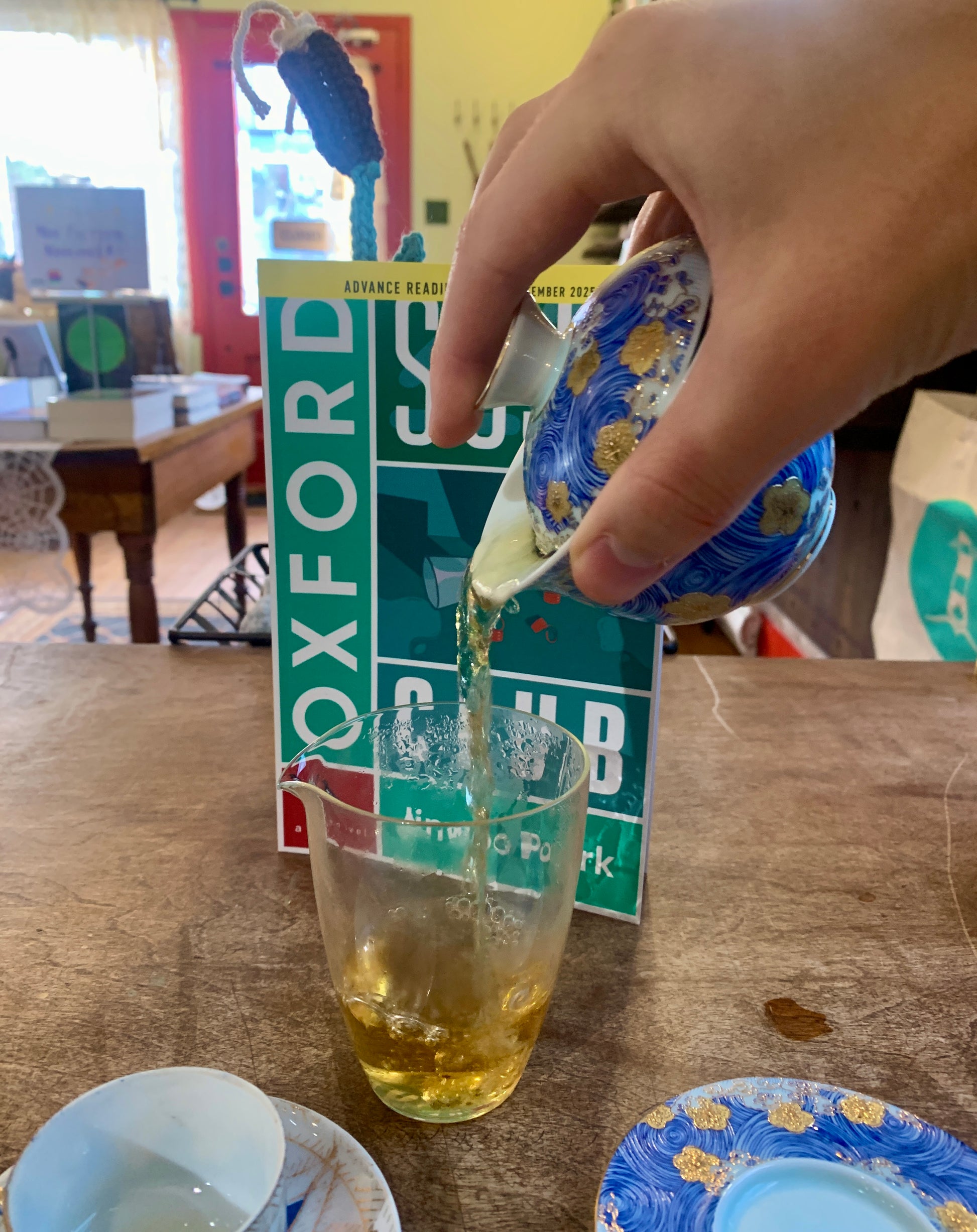 Hand pouring tea into a glass on a table with an Oxford English Dictionary in the background.