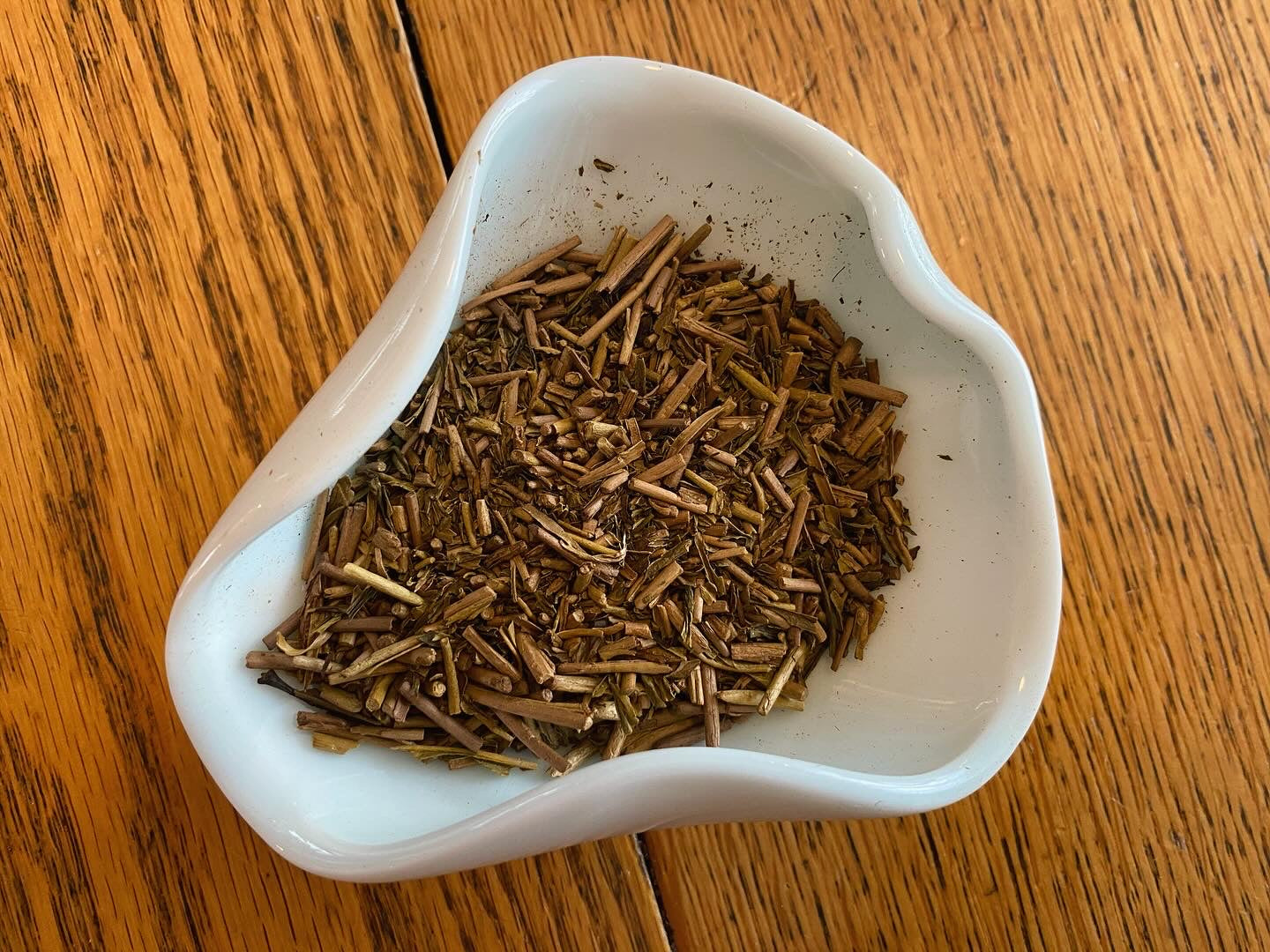 A white bowl filled with Hojicha green tea, showcasing its dried leaves.