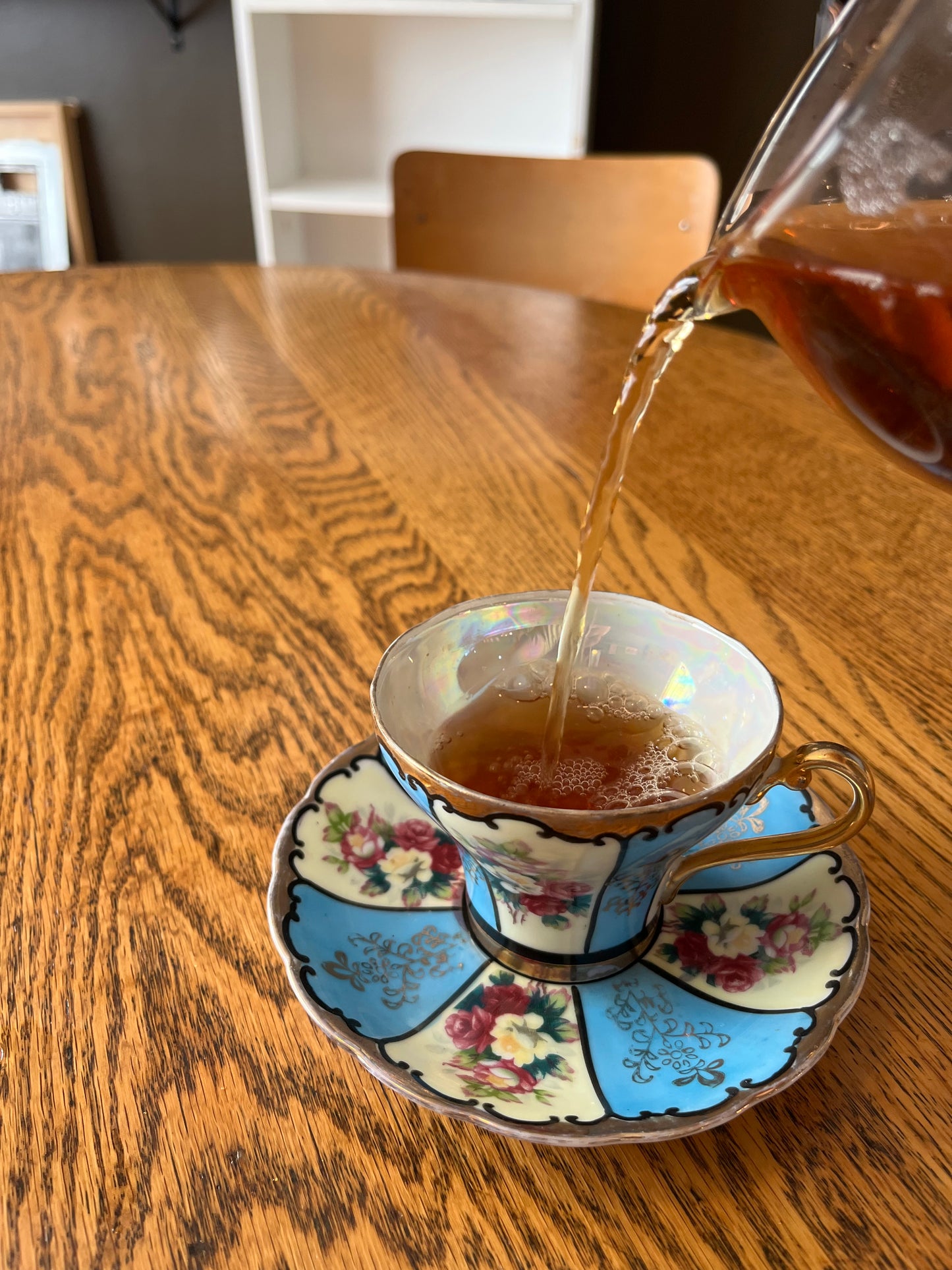 Tea cup with floral design being filled with a malty tea on a wooden surface