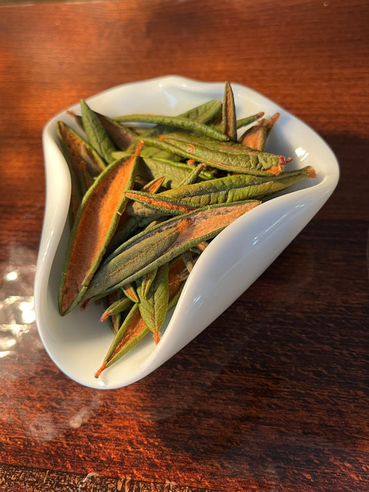 Labrador Tea leaves in a white dish on a wooden surface