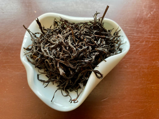 A cup of loose Lapsang Souchong tea leaves, with a smoky flavor, displayed on a wooden surface.