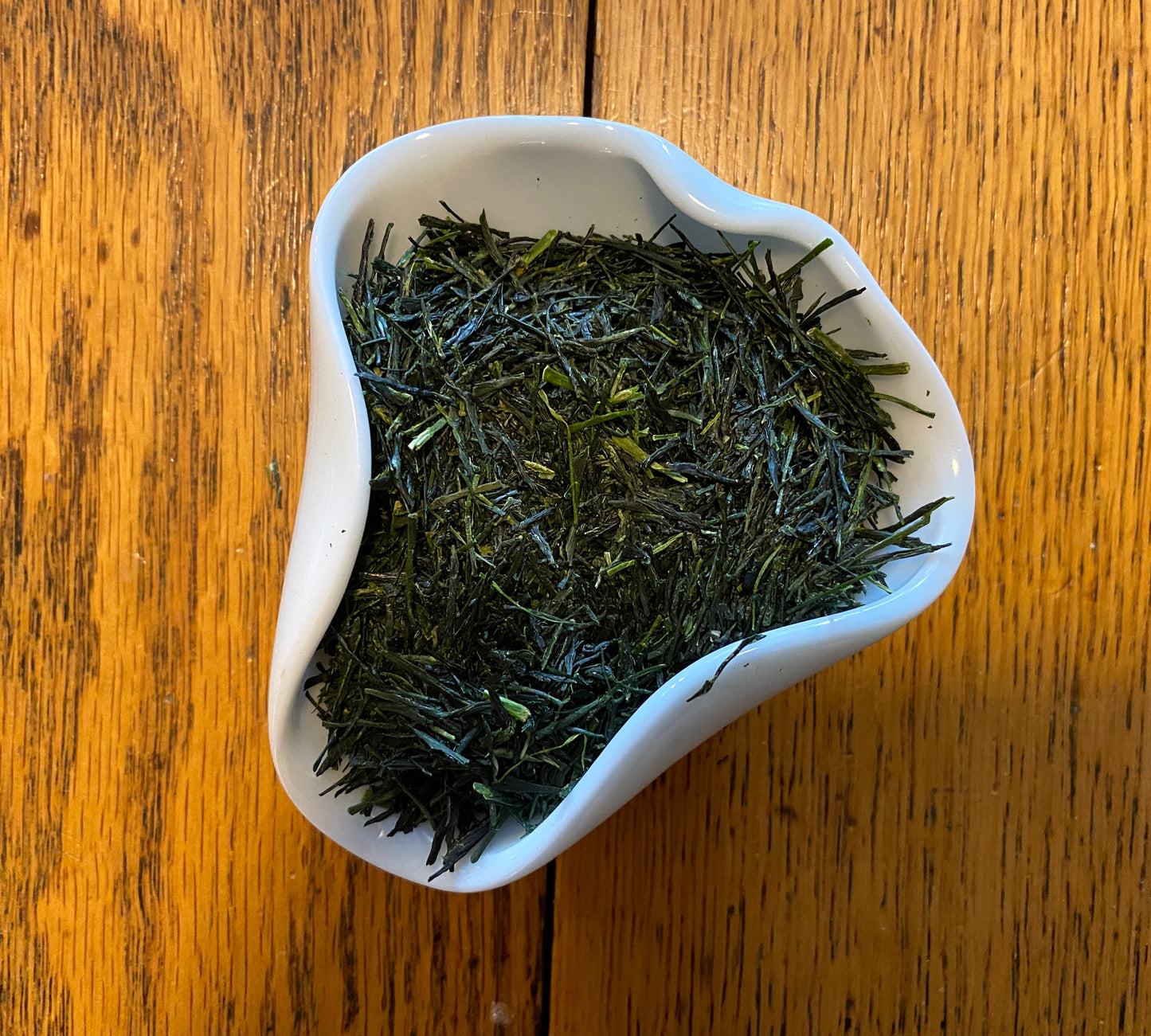 A white cup filled with green tea leaves on a wooden surface.