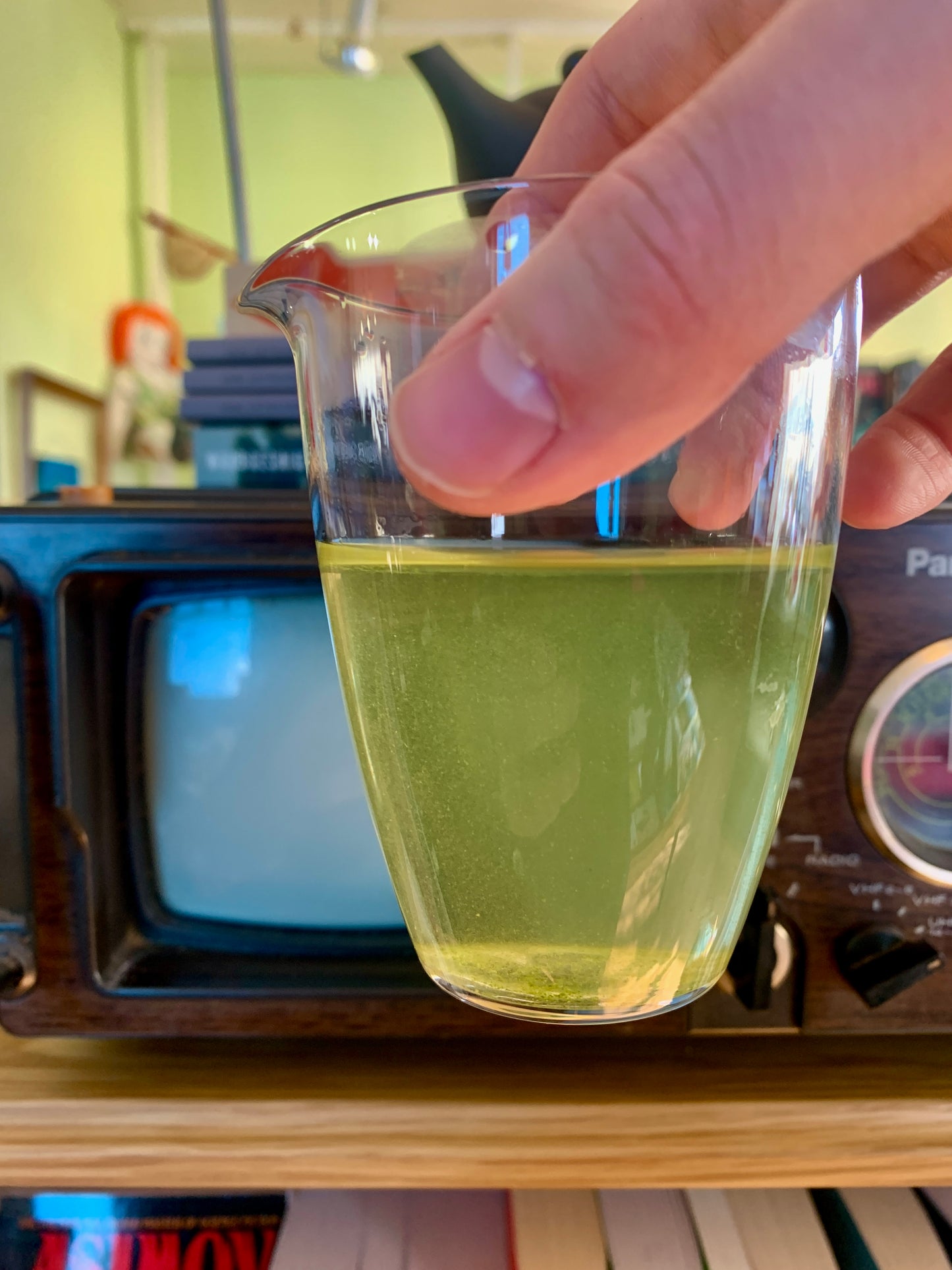 Hand holding a glass of green tea in front of an old television set.