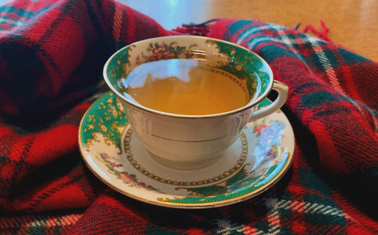 A cup of tea with a floral pattern on the cup on a tartan plaid blanket